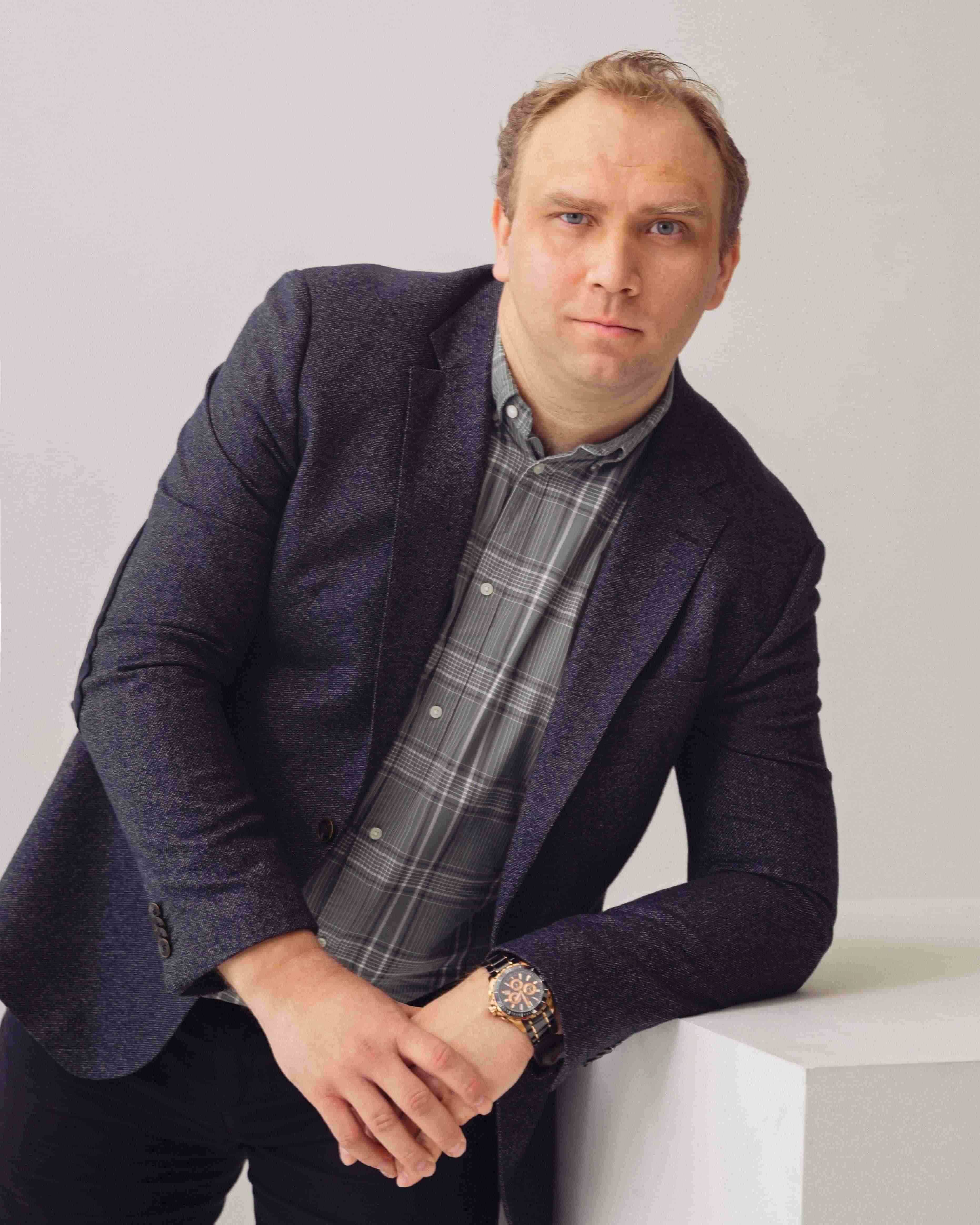 Владимир Болонкин, директор компании Инмако, мужчина в синем пиджаке и клетчатой рубашке опирается на белый куб 