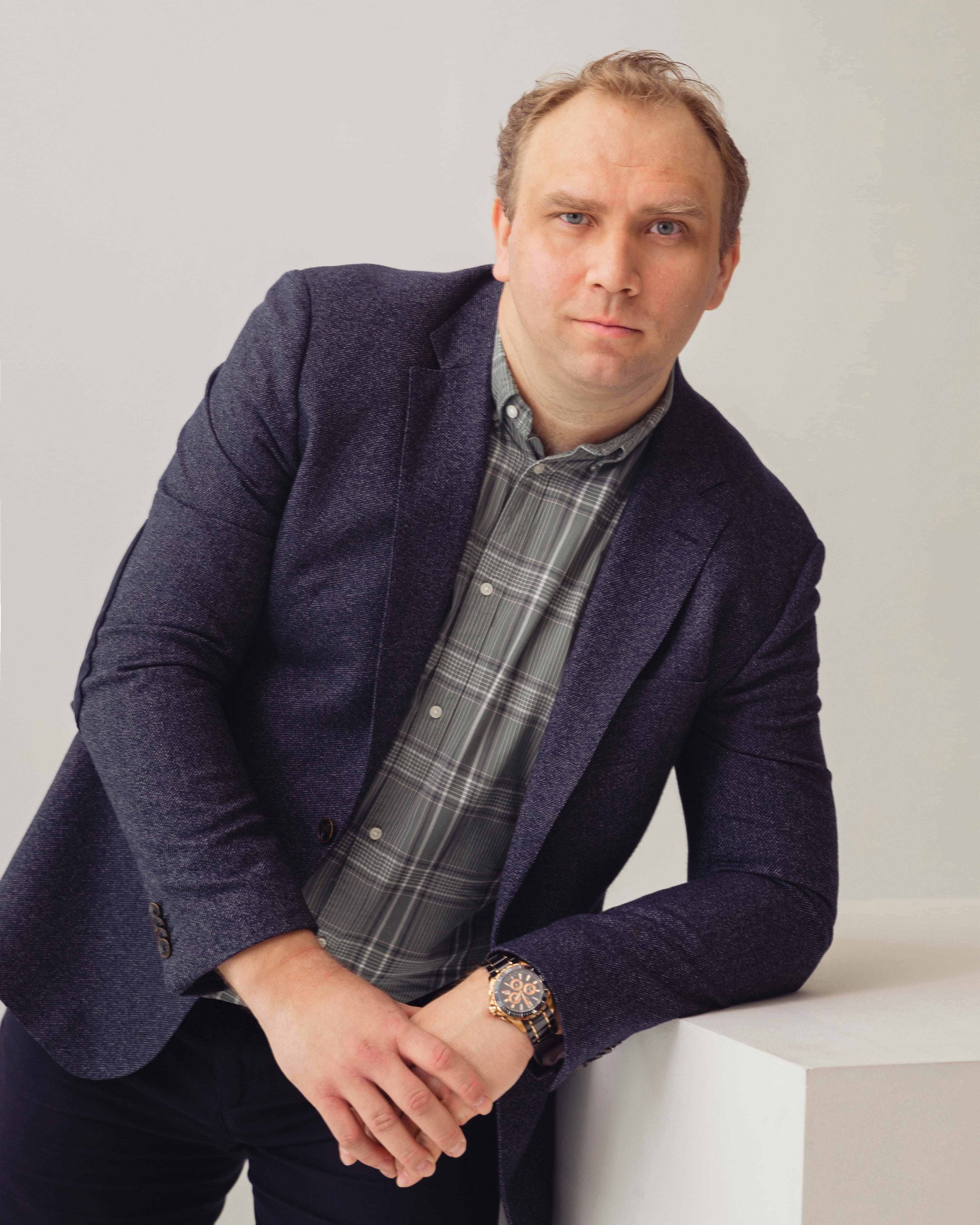 Владимир Болонкин, директор компании Инмако, мужчина в синем пиджаке и клетчатой рубашке опирается на белый куб 